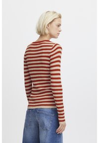 Rot und beige gestreifter Rippstrickpullover mit langen Ärmeln und rundem Ausschnitt, kombiniert mit blauen, hochtaillierten Jeans aus Denim.