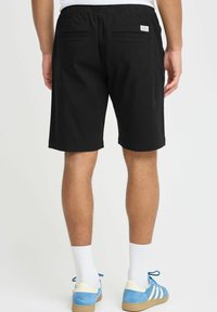 Sorte bomullsshortser med elastisk midje, to baklommer og rett snitt. Brukt med blå sneakers og hvite sokker.