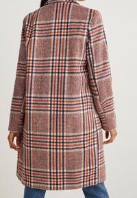 Abrigo trench de cuadro en tejido suave con colores rojo, marino y crema. Detalles destacados incluyen un cuello con muesca y bolsillos laterales.