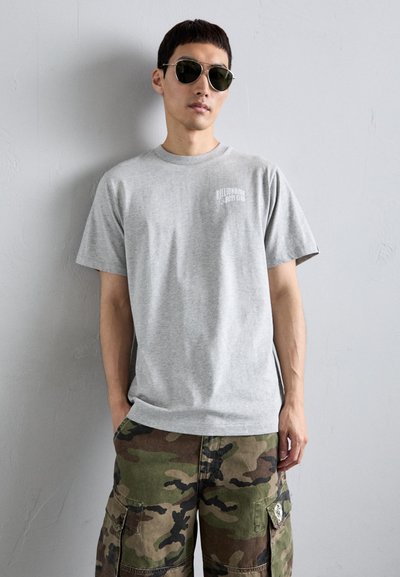Tricou gri din bumbac cu mâneci scurte și guler rotund, având un mic logo alb pe piept. Purtați cu pantaloni scurți cargo cu model de camuflaj.