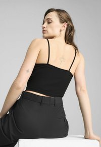 Čierny kvetinkový crop top s tenkými ramienkami, kombinovaný s čiernymi vysokými nohavicami. Disponuje jemným tetovaním na zadnej strane a minimalistickým štýlom.