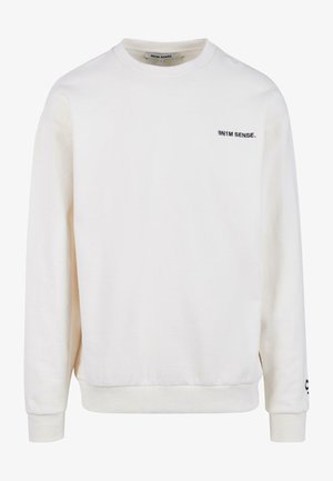 Krém színű pulóver, puha anyagból készült, kerek nyakkivágással és bordás mandzsettákkal. A bal mellen egy kis fekete logo található.