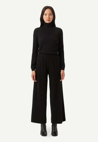 Svart polotröja och vida byxor i mjukt tyg. Outfiten kompletteras av svarta ankelskor.