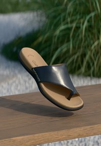 Sandale bleu foncé, brillante, avec une boucle pour les orteils et une large sangle. Semelle intérieure en cuir tan rembourrée, conception légère et accents de couture décoratifs.