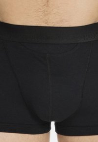 Nahaufnahme eines Mannes, der schlichte schwarze Boxershorts mit elastischem Bund und sichtbaren Nähdetails trägt.