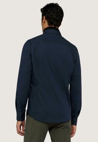 Camicia a maniche lunghe blu navy con una texture liscia, polsini abbottonati e colletto classico, che presenta un sottile design del retro.