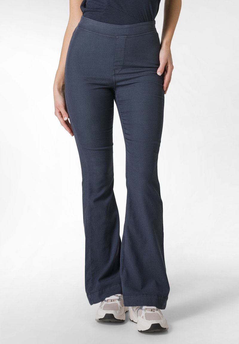 Námořnické modré kalhoty s rozšířením a hladkým povrchem, s elastickým pasem, s přiléhavým střihem, který sahá až na zem, doplněné o světlé tenisky.