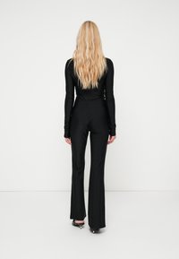 Musternädalane must kombinesioon, millel on sobiv torso ja laienevad püksid, sile tekstuur ja lihtne disain. Ümber on mustad kõrge kontsaga kingad.