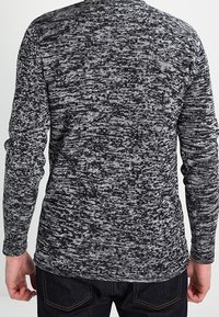 Maglietta a maniche lunghe lavorata a maglia in un motivo mélange bianco e nero. Presenta un collo rotondo e maniche aderenti, realizzata in un morbido tessuto testurizzato.