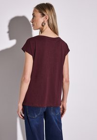 Camiseta marrón con mangas cortas enrolladas, escote redondo, corte relajado, hecha de tela suave, combinada con jeans azul oscuro.
