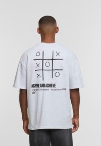 T-shirt grigio in cotone con design a tris e testo sul retro. Vestibilità ampia con maniche corte e scollatura a girocollo.