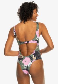 Maillot de bain une pièce vert avec un motif floral comprenant des fleurs roses et blanches. Design à dos découpé, bretelles larges et texture lisse.