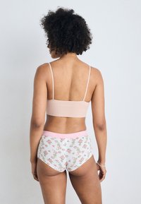 Svijetloružičasti rebrasti bralette uparen s bijelim gaćicama s cvjetnim uzorkom i ružičastim pojasom. Mekani materijali i prilagođeni dizajn.