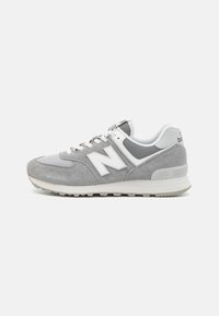 Šedé a bílé tenisky New Balance s svrchním materiálem z semiše a síťoviny, bílé šněrování a gumová podrážka na světlém pozadí.