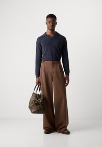 Navy long-sleeve polo with a V-neck, brown wide-leg trousers, and a green bag with brown accents. Footwear is dark brown. Simple, modern design.