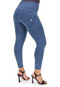 Leggings in denim blu, a vita alta, con una superficie liscia e tasche posteriori decorate, impreziosite da un logo dorato. Indossati con tacchi neri.