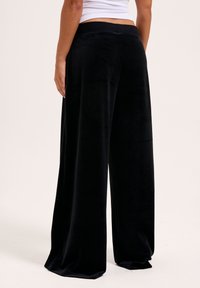 Schwarze Samt-Hose im weiten Schnitt mit glatter Textur, hohem Bund und lockerer Passform, die ein fließendes Design von der Taille bis zum Saum zeigt.