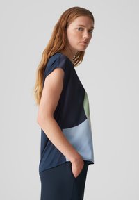 Top corto a maniche corte di colore blu navy con blocchi di colore circolari in verde chiaro e blu. Tessuto morbido, vestibilità rilassata con tasche laterali.