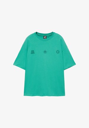 T-shirt vert à manches courtes avec petit texte noir "Never Ending Sunsets," "1991," et un graphisme de soleil sur la partie supérieure de la poitrine.