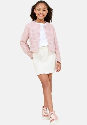 Veste en tweed rose avec encolure ronde et fermetures à boutons, associée à un t-shirt blanc et une mini jupe crème. Baskets montantes roses.