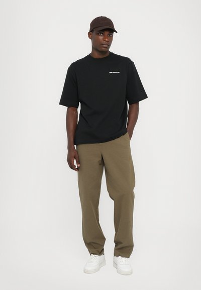 Tricou negru cu mâneci scurte, având un mic design de text alb. Asortat cu pantaloni khaki și adidași albi. Sapcă maro pe cap.
