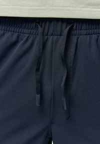 Marine mesh shorts met een elastische tailleband, voorzien van een trekkoord met zwarte uiteinden, gecombineerd met een lichtgroene T-shirt daarboven.