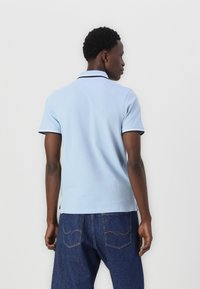Lys blå polo skjorte med krave, korte ærmer og kontrast sort kant. Båret med mørke denim jeans, der viser et afslappet fit.