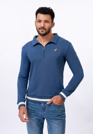Blue zip-up sweatshirt with a collar, featuring a small golden logo on the chest, white striped cuffs, and a ribbed hem. Casual design.