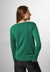 Grünes Langarmshirt mit lässigem Schnitt und gerippter Textur. Verfügt über einen weiten Ausschnitt und schmale Ärmel, kombiniert mit dunklen Jeans.