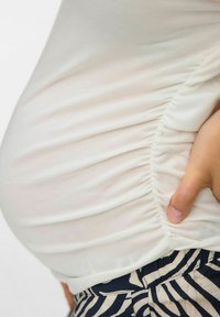Hvid samlet top lavet af blødt, strækbart stof, parret med mørk mønstret bunden med cremede striber mod en marineblå baggrund.