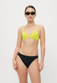 Gul trekantet bikini topp med halterstropper og en svart bikini-bunn med utskårne detaljer på sidene. Glatt, matt stoff.
