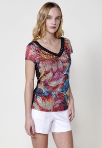 Blusa de mangas cortas multicolor con cuello en V negro, que presenta un patrón texturizado y vibrantes diseños florales en rojo, azul y amarillo.