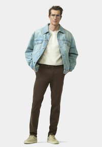 Veste en denim bleu clair, pull beige, pantalon slim marron et baskets beige. La veste présente des poches et des boutons classiques.
