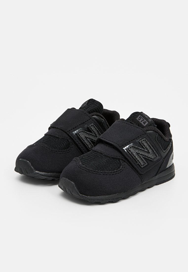 Baskets de sport noires avec tige en mesh, bandes Velcro et semelle en caoutchouc. Présente le logo New Balance en matériau réfléchissant.
