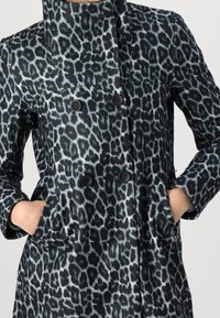 Cappotto con stampa leopardata, colletto alto, design doppiopetto e bottoni neri. Presenta tasche laterali e un tessuto morbido e testurizzato.