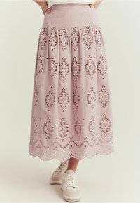 Rosa bomullsmidijort med broderade hålmönster, en samlad midja och en vågig fåll, kombinerad med vita sneakers.