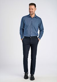 Napapaita tummansinisestä kankaasta, jossa on tasku ja kuvioitu kaulus, yhdistetty tummiin housuihin ja mustiin kenkiin.