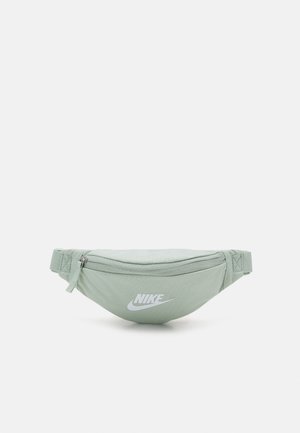 Jasnozielona nerka Nike z przednią kieszenią na zamek i regulowanym paskiem, z białym logo Nike na przednim środku.