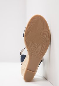Semelle d'une sandale compensée pour femme avec une semelle en caoutchouc texturée et taille 37, montrant un talon en jute tissé et une bride en tissu bleu marine.