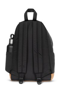 Mochila de tela negra con correas acolchadas, un asa en la parte superior y un bolsillo lateral que sostiene una botella de agua negra. Detalle inferior en un material similar al cuero en color marrón.