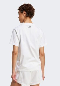 Vit bomull t-shirt med korta ärmar, utan detaljer på framsidan, och liten svart Adidas-logga på övre baksidan. Bärs med matchande vita shorts.