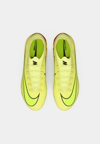 Zapatos de fútbol amarillos con un acabado texturizado, que presentan acentos en negro y un distintivo swoosh de Nike. Los cordones son visibles, con un diseño de ajuste ceñido.