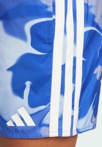Pantaloni sportivi blu caratterizzati da un motivo astratto a spirale, tre strisce bianche lungo il lato e un logo Adidas bianco sull'orlo.