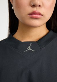 Black short-sleeve shirt featuring a textured collar and a silver embroidered Jumpman logo on the neckline.