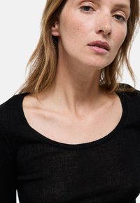 Haut noir à c�ôtes avec un décolleté large. Le tissu semble léger et texturé, laissant légèrement entrevoir la peau en dessous.