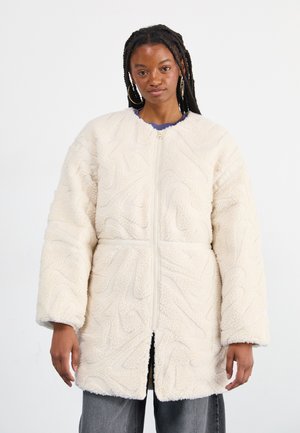 Veste en polaire couleur crème avec un motif texturé en vagues, fermeture éclaire et manches larges. Présente une coupe décontractée et un matériau doux et pelucheux.
