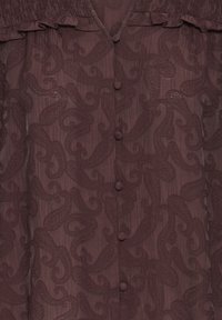 Tissu marron foncé transparent avec broderie cachemire et boutons recouverts au centre, avec un bord froncé à volants en haut.