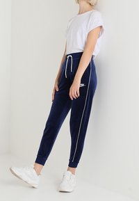 Námořnické modré velurové tepláky s bílými postranními pruhy a elastickým pasem, doplněné bílým tričkem s krátkým rukávem a bílými teniskami.