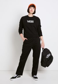 Sudadera negra con el logo "VANS", pantalones negros y zapatillas negras con acentos blancos. Gorro naranja y mochila negra.
