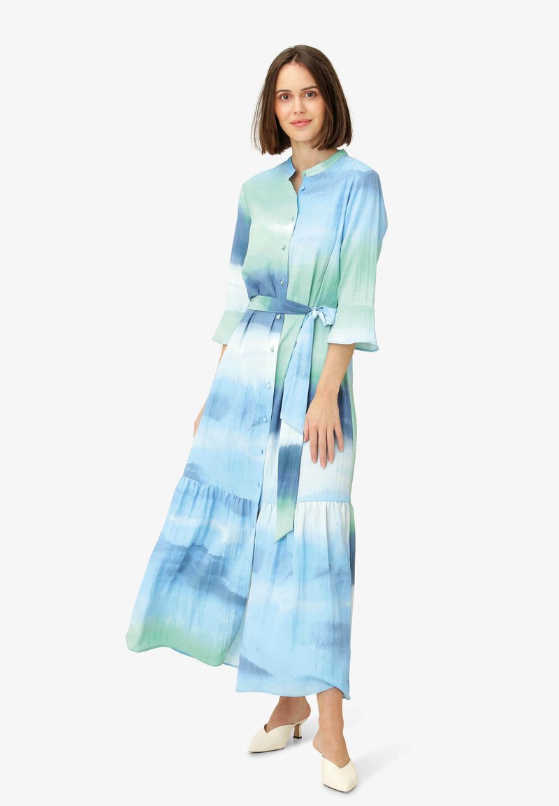 Rochie lungă cu un model gradient în nuanțe de albastru și verde. Fabricată dintr-un material fin, cu un sistem de închidere tip buton, curea legată și un design stratificat.
